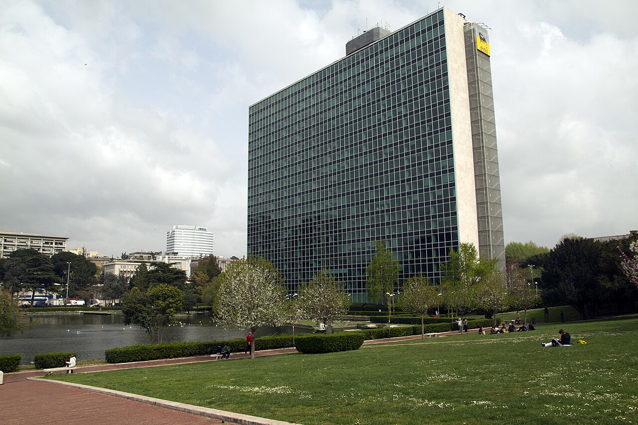 Edificio de oficinas de gran altura con fachada de vidrio rodeado por un parque verde.