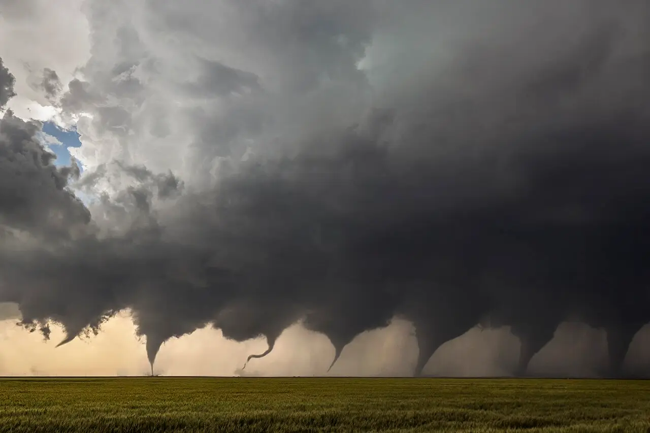 Un tornado se forma sobre un campo verde bajo un cielo oscuro y tormentoso.