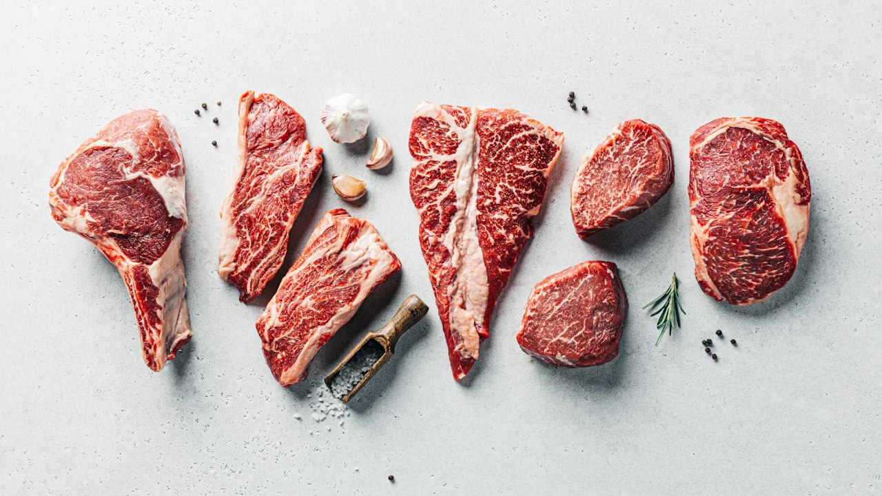 Diversos cortes de carne vacuna cruda con especias sobre una superficie de concreto gris.