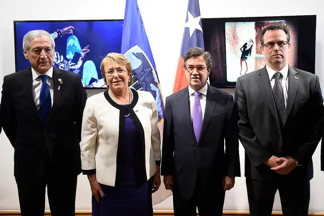 Cuatro personas con traje posan formalmente frente a las banderas de Chile y el BID.