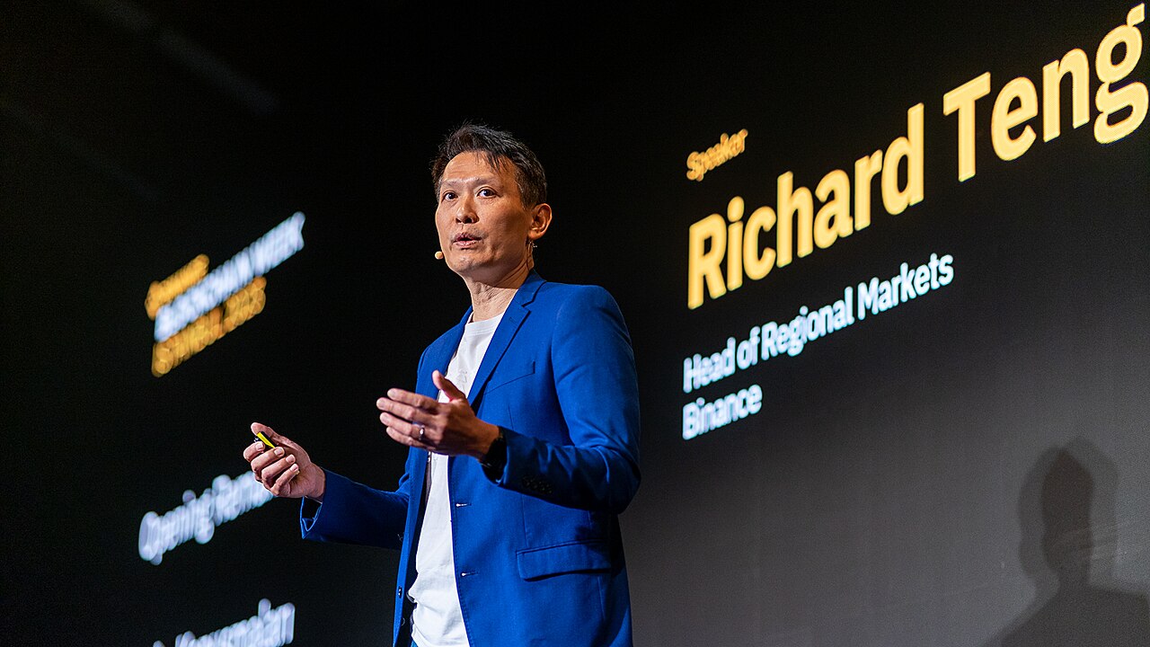 Richard Teng gesticula mientras expone en un evento corporativo frente a una pantalla negra.