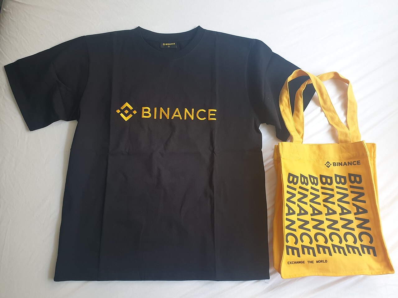 Una remera negra y una bolsa de tela amarilla con el logotipo de Binance.