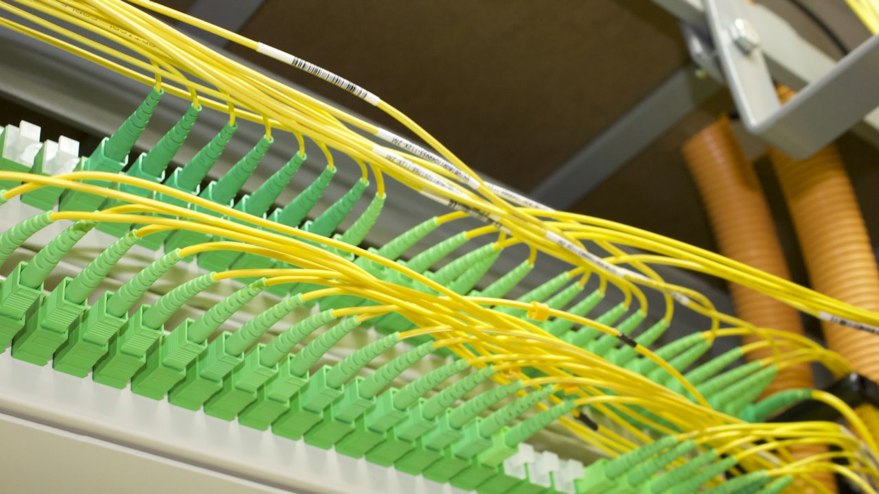 Conexiones de fibra óptica con cables amarillos y verdes en un panel de red.