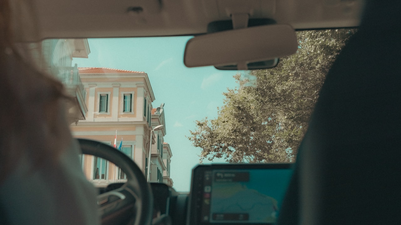 Vista desde el interior de un vehículo circulando por una calle con arquitectura europea antigua.
