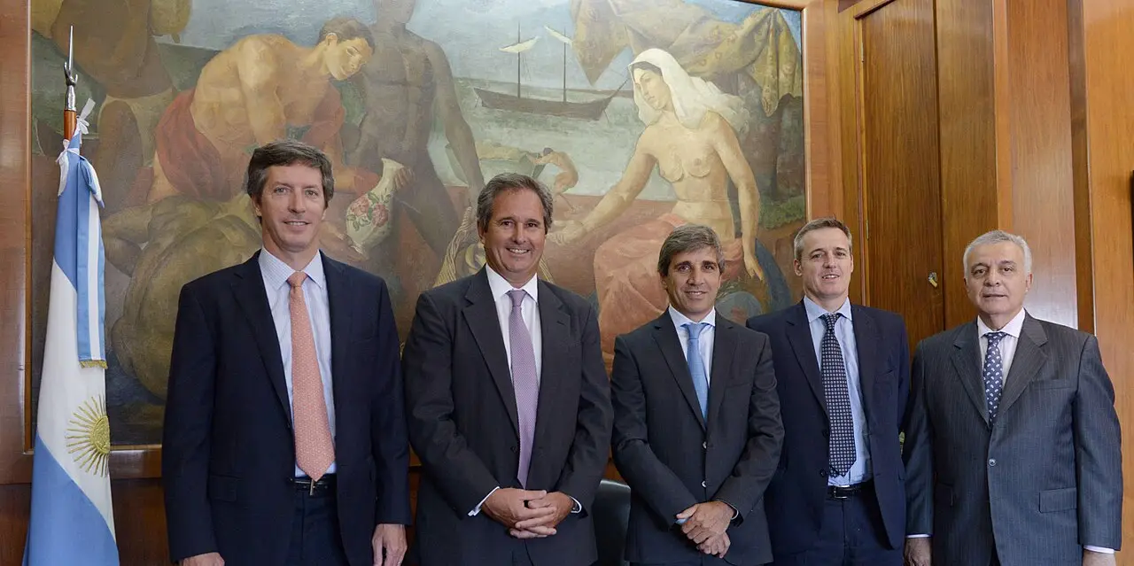 Luis Caputo posa junto a otros funcionarios frente a una bandera argentina y un mural.
