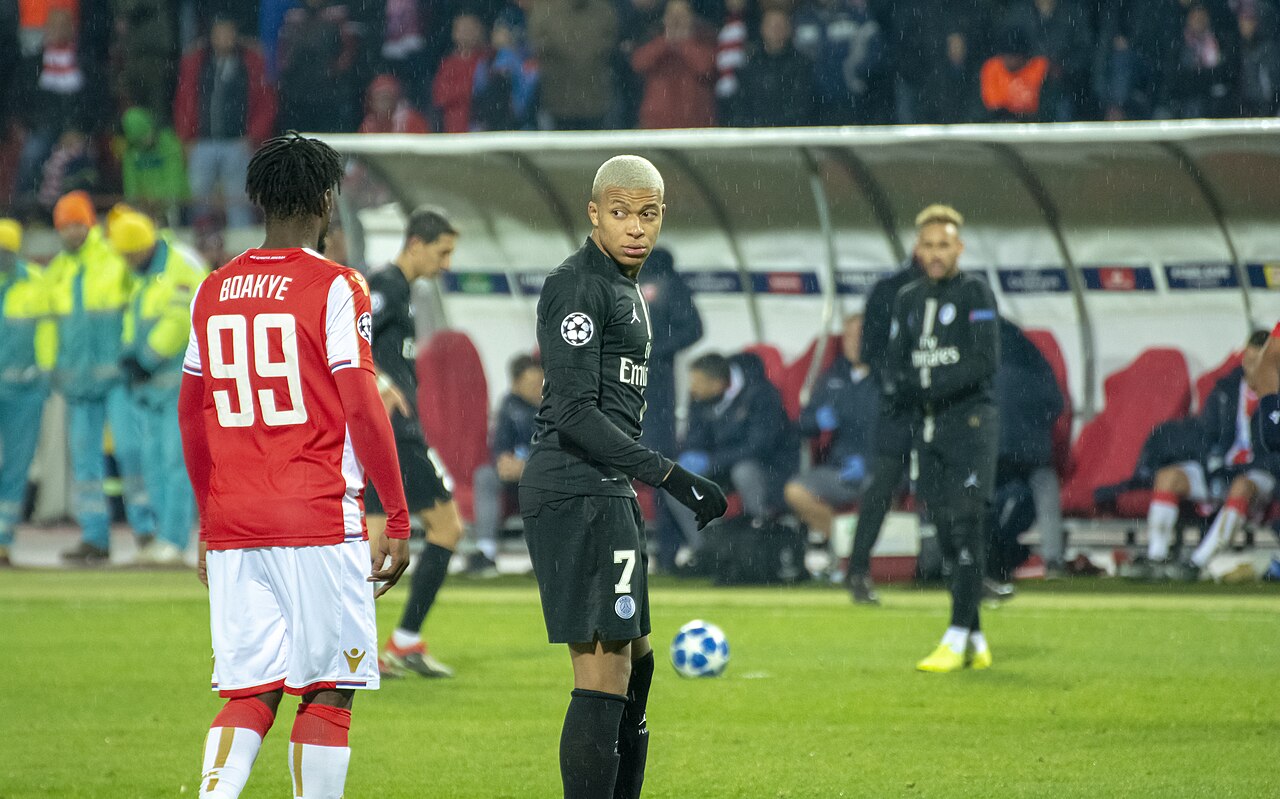 Kylian Mbappé con la camiseta negra durante un partido de fútbol profesional en un estadio.