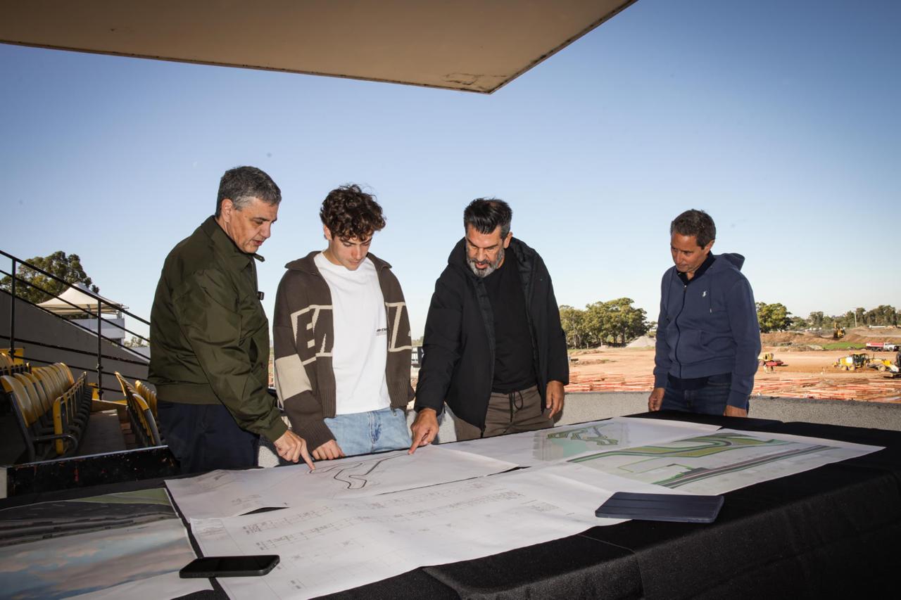 Franco Colapinto observa planos sobre una mesa junto a otras personas al aire libre.