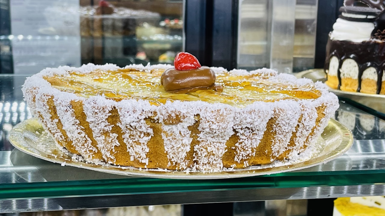 Un alfajor artesanal con bordes de coco rallado y una cereza en la parte superior.