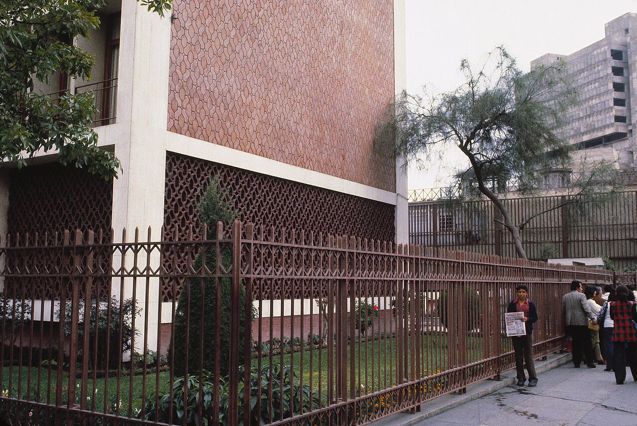 Fachada de un edificio institucional en Lima con personas caminando por la vereda cercana.