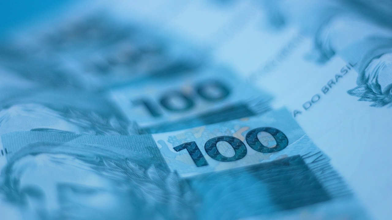 Primer plano de billetes de cien dólares estadounidenses apilados sobre una superficie azul.