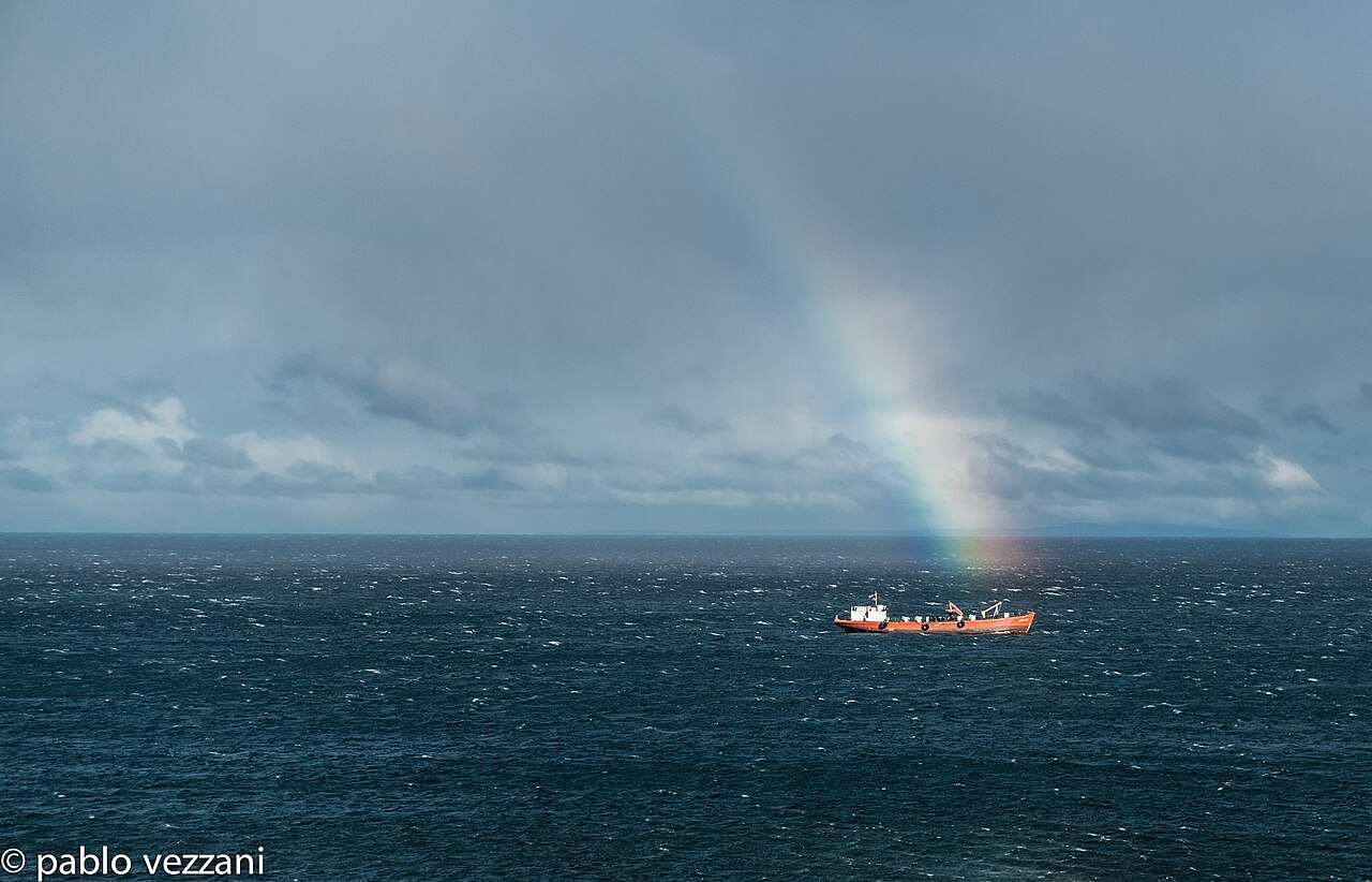 Un barco navega por las aguas del Estrecho de Magallanes bajo un arcoíris.