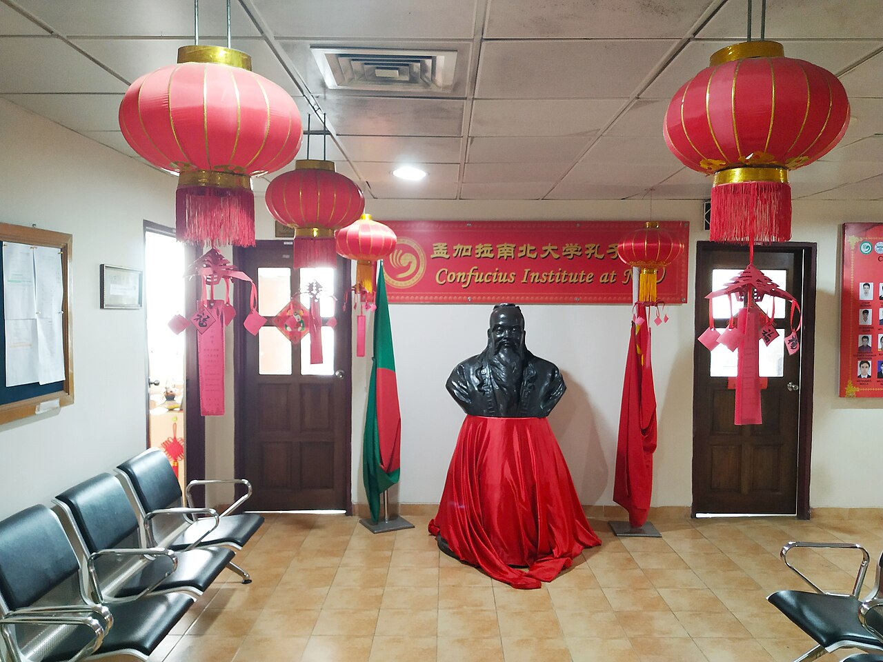 Busto de Confucio decorado con telas rojas y farolillos chinos en una sala universitaria.