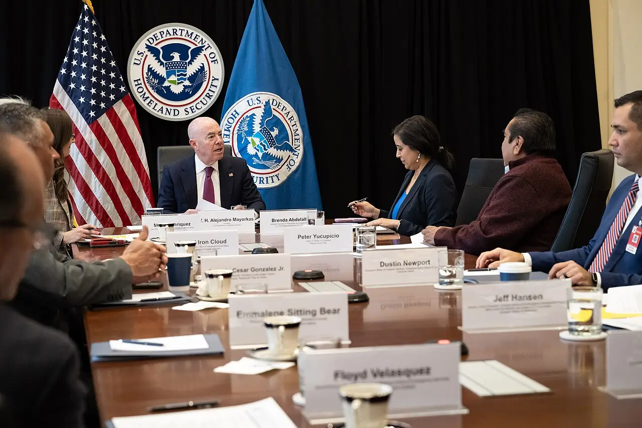 Funcionarios estadounidenses debaten políticas migratorias sentados alrededor de una mesa de conferencias con banderas oficiales.