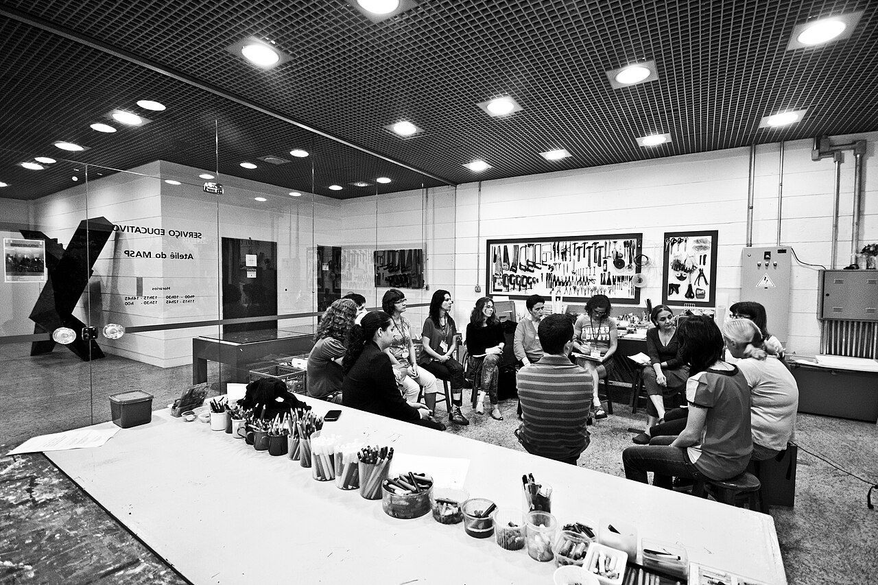 Varias personas participan en una reunión cultural en un amplio salón iluminado en Sao Paulo.