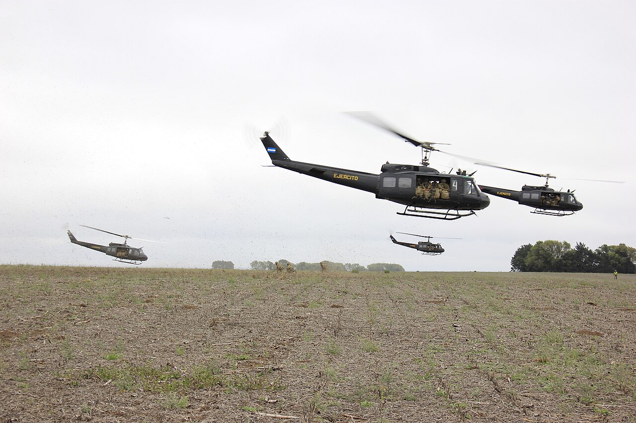 Varios helicópteros Bell UH-1 del Ejército Argentino vuelan en formación sobre un campo abierto.