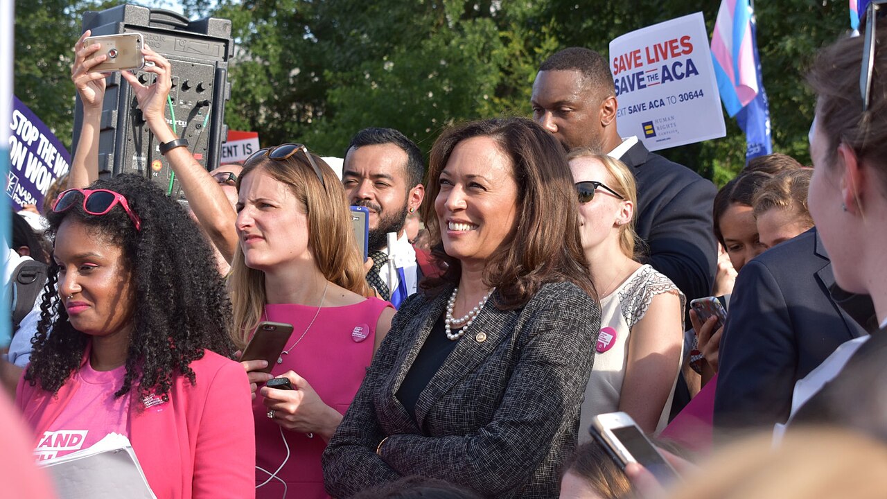 Kamala Harris sonríe rodeada de personas en una manifestación pública al aire libre.