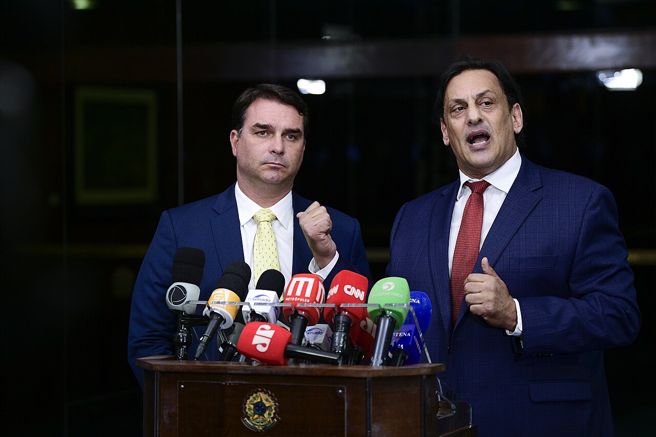 El senador Flávio Bolsonaro junto a su abogado durante una conferencia de prensa con micrófonos.