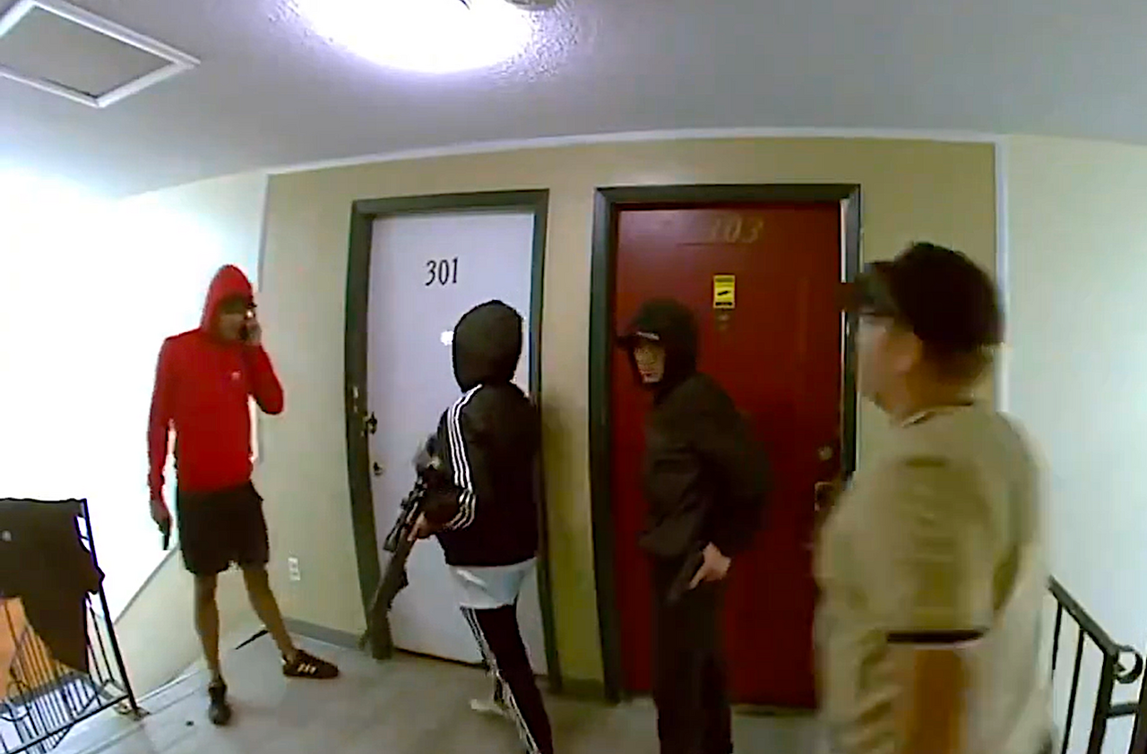 Grupo de personas con vestimenta oscura y armas en un pasillo de edificio residencial.