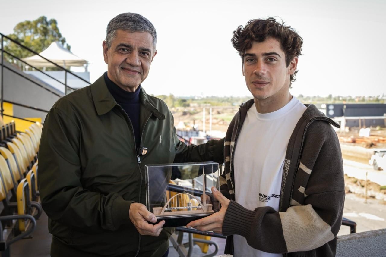 El piloto argentino Franco Colapinto sostiene un pequeño objeto decorativo junto a un hombre mayor.