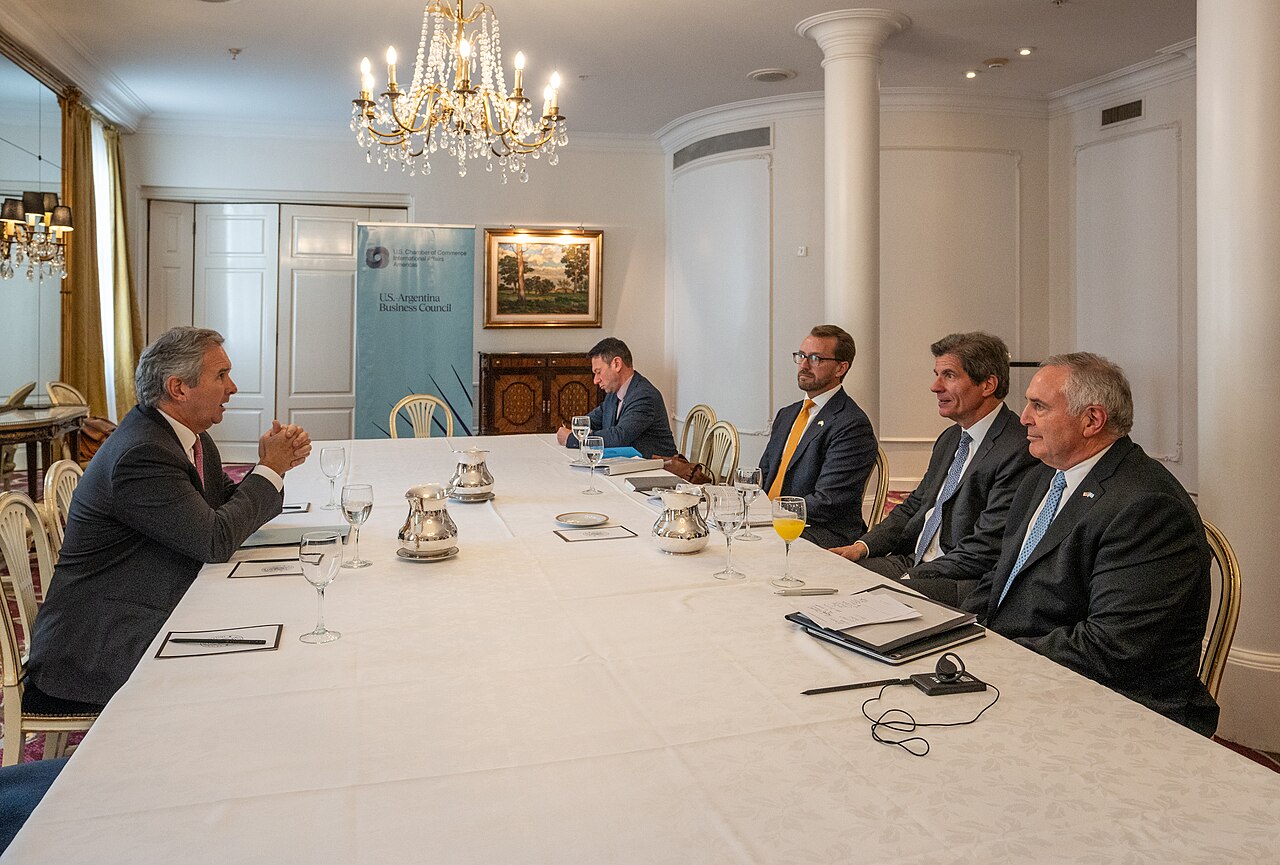 Funcionarios gubernamentales reunidos alrededor de una larga mesa blanca en una sala elegante.