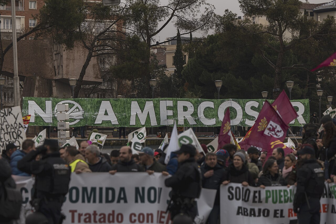 Una multitud de manifestantes sostiene pancartas y banderas con consignas contra el acuerdo comercial.