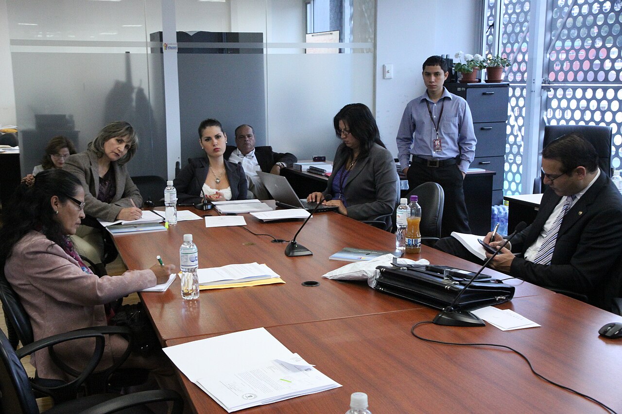 Un grupo de funcionarios y profesionales reunidos alrededor de una mesa de trabajo en una oficina.
