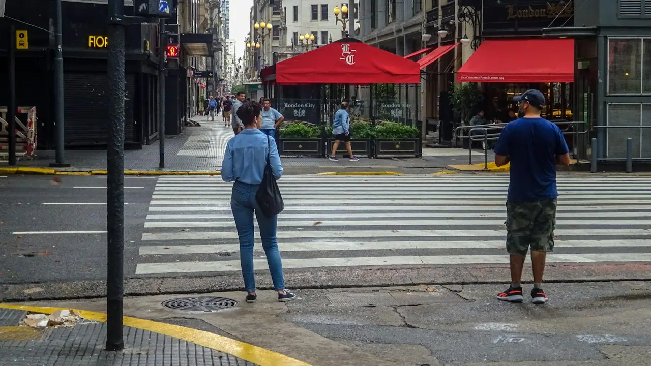 Personas cruzan una calle comercial de Buenos Aires con locales gastronómicos de fondo.