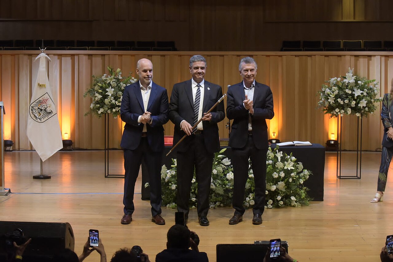Jorge Macri en un acto oficial junto a otras autoridades en un escenario con flores.