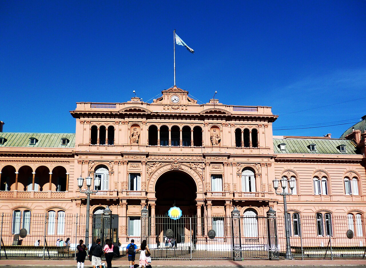 Vista frontal de la Casa Rosada con la bandera argentina flameando bajo un cielo despejado.