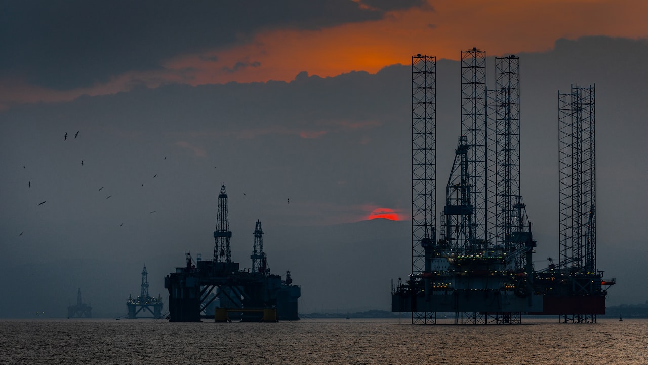 Plataformas petroleras en el mar durante el atardecer bajo un cielo nublado y oscuro.