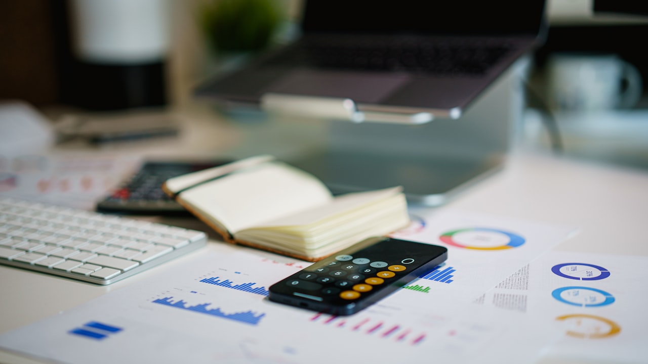 Una calculadora y gráficos financieros descansan sobre un escritorio junto a una computadora portátil.