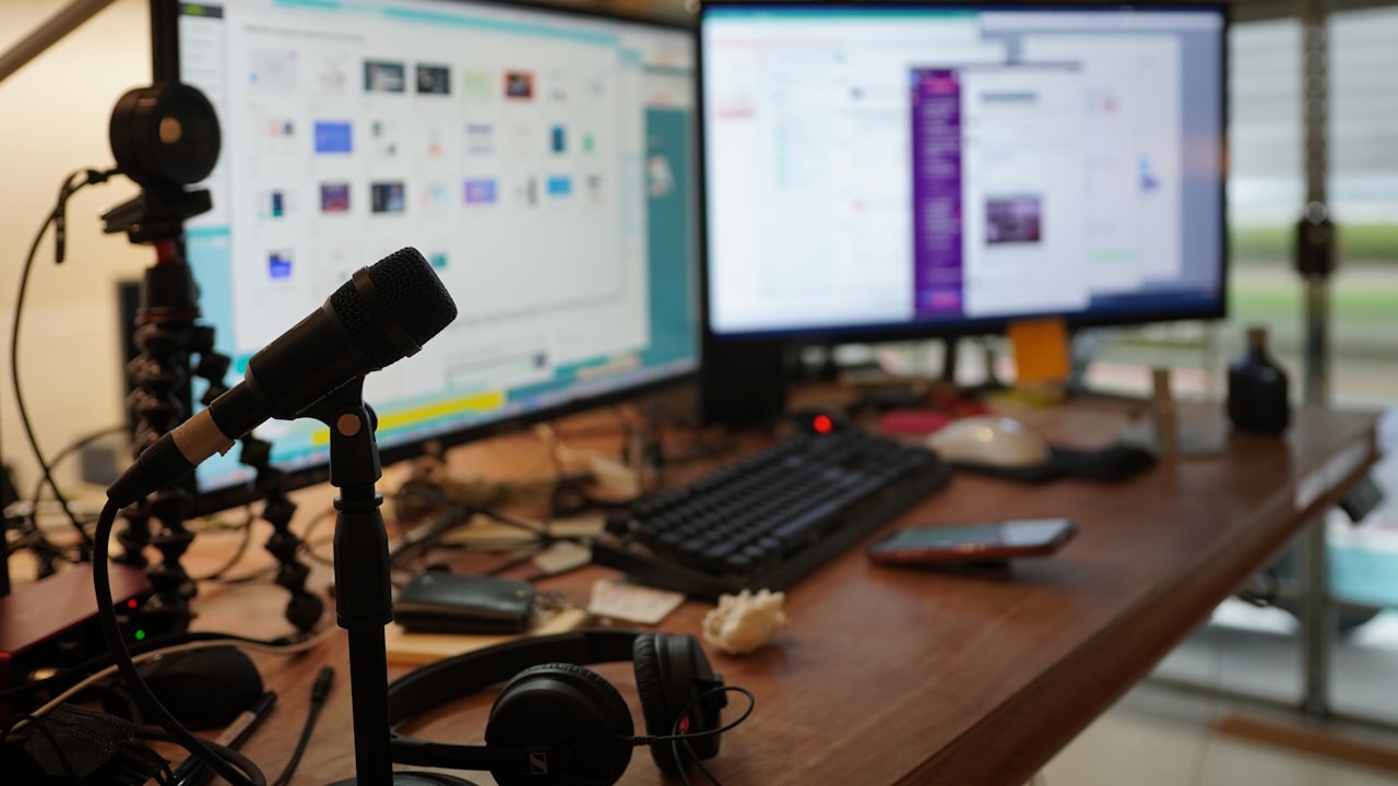 Un escritorio con dos monitores encendidos, un micrófono y auriculares en un espacio laboral.