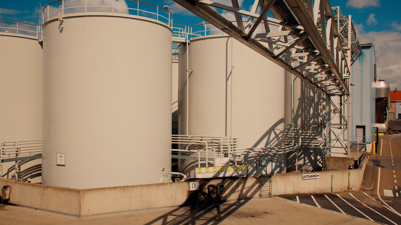 Tanques de almacenamiento de petróleo en una planta industrial con estructuras metálicas y tuberías visibles.