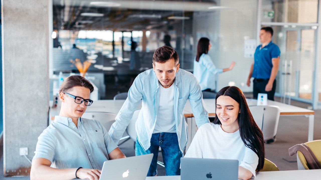 Tres jóvenes profesionales trabajan juntos frente a computadoras portátiles en una oficina moderna y luminosa.