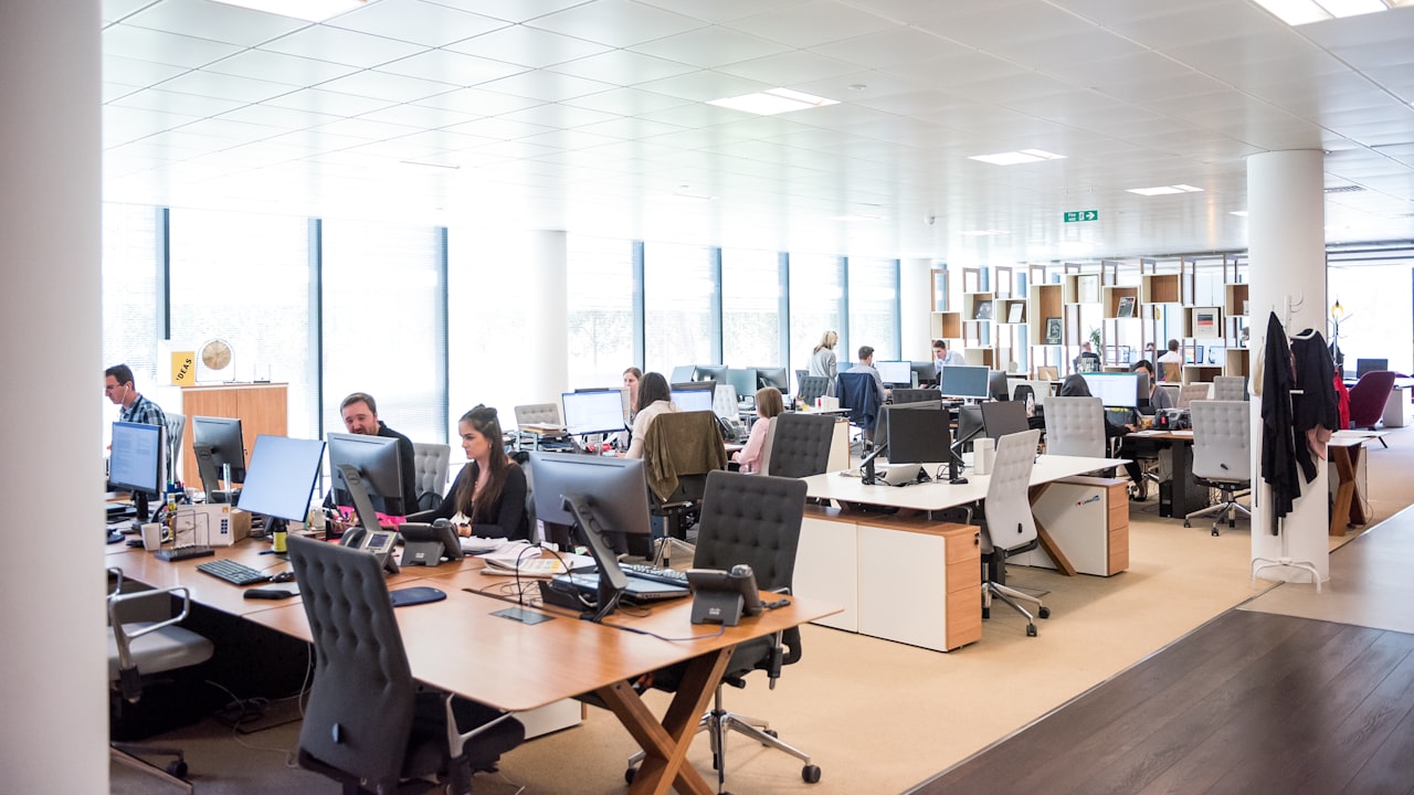 Vista panorámica de una oficina abierta con varios empleados trabajando en sus escritorios individuales.