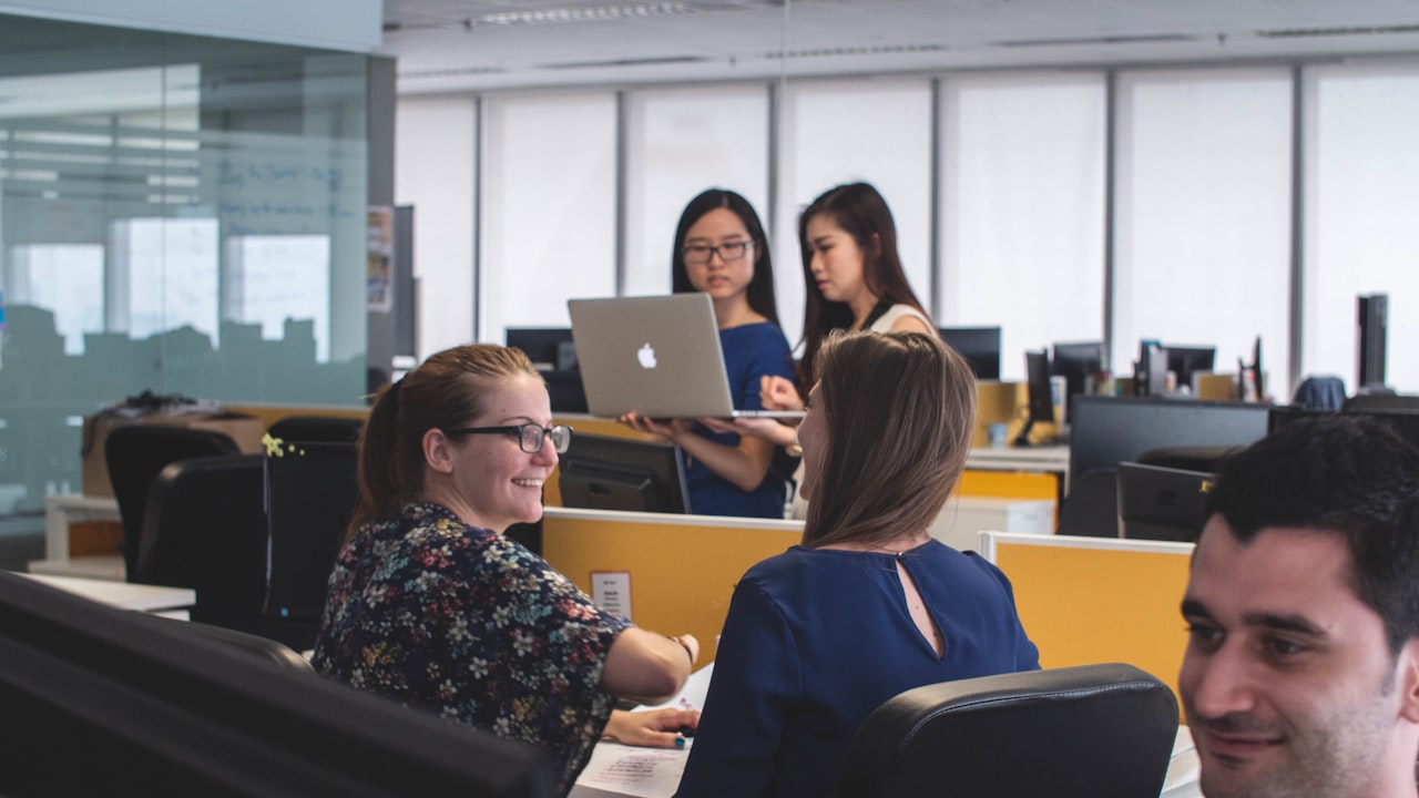 Grupo de personas trabajando en una oficina corporativa con computadoras y escritorios compartidos.