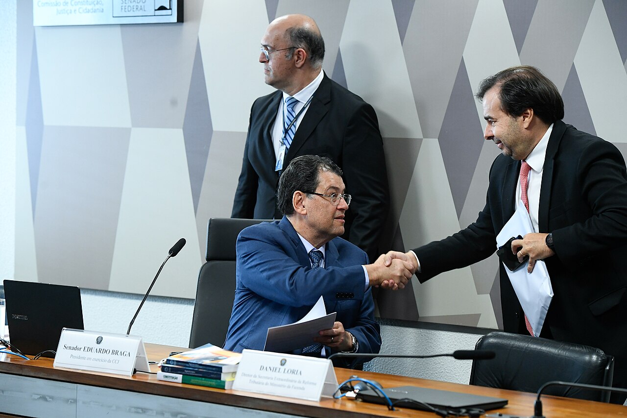 Dos hombres se dan la mano en una mesa de trabajo dentro del Senado nacional.
