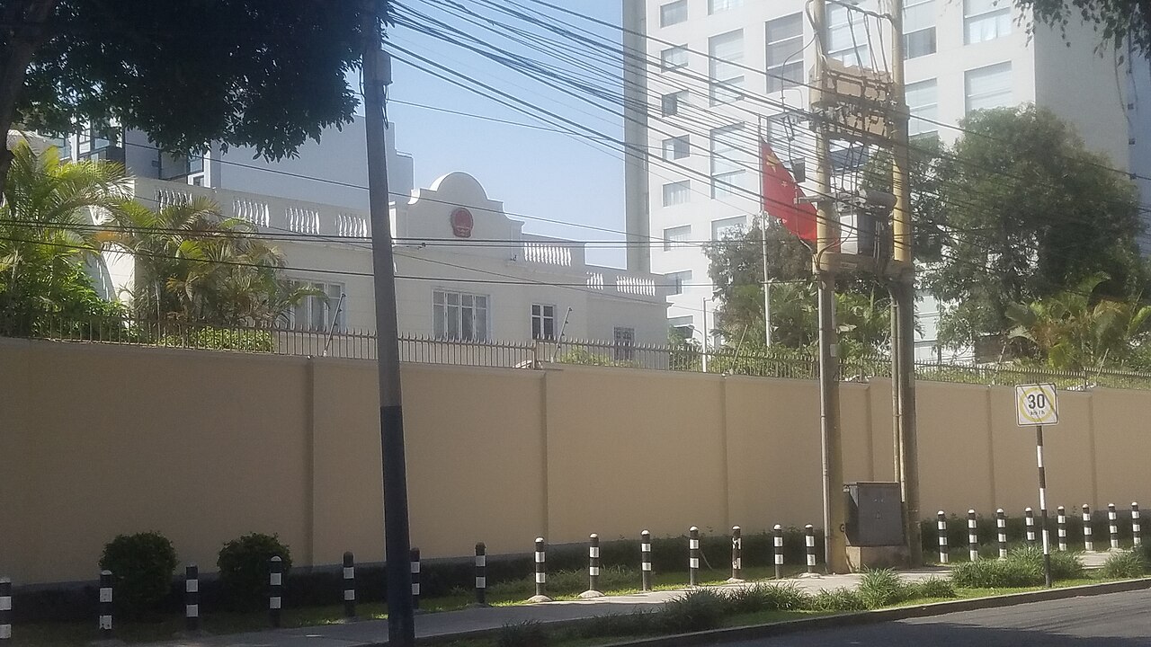 Fachada de la sede diplomática china con un muro perimetral y vegetación en la calle.